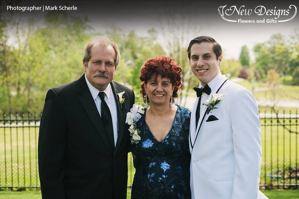 A groom stands with his parents, sporting gorgeous boutonnieres and a corsage of calla lillies and orchids.